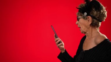Komik, yaşlı bir kadın çerçevede yürürken akıllı telefonundan biriyle konuşuyor. Duruyor ve kareye doğru devam ediyor. Kırmızı arkaplanda izole