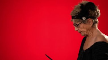 Akıllı telefonuyla kayarken komik yaşlı kadın karede yürür durur, durur, gülümser ve karede yürümeye devam eder. Kırmızı arkaplanda izole