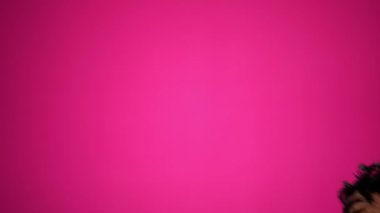 Gülen yaşlı bir kadının komik portresi. Peruk takıyor ve pembe arka planda sabahlık giyiyor..