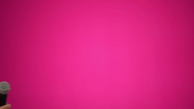Gülen yaşlı bir kadının komik portresi. Peruk takıyor ve pembe arka planda sabahlık giyiyor..