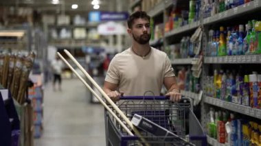 Hırdavatçıda alışveriş arabasını iten mutlu genç adamın ön görüntüsü.