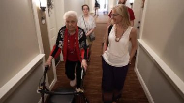 Yaşlı yaşlı bir anne, bir yürüteç kullanıyor, kızı, torunu ve kız arkadaşı tasmalı köpeğiyle bir aile ziyareti sırasında huzurevine asansörle gidiyor..
