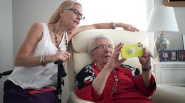 Kızı ve yaşlı annesi telefondaki fotoğraflara bakıp gülümsüyor ve işaret ediyor..