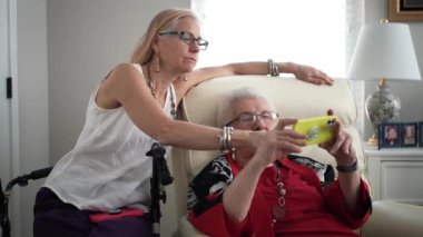 Kızı ve yaşlı annesi telefondaki fotoğraflara bakıp gülümsüyor ve işaret ediyor..