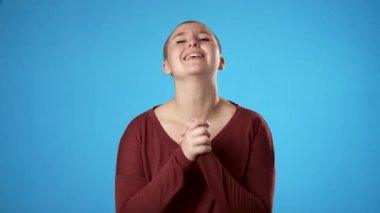 Dua ederken el ele tutuşup bir şey dilerken parmaklarınızı çapraz yapın. Çift cinsiyetli olmayan genç kadın 20 'li yaşlarda mavi arka plan stüdyosunda izole..