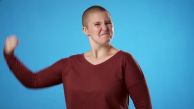 Çift cinsiyetli olmayan, 20 'li yaşlarda, gösteri kaslı genç bir kadının portresi. Stüdyoda mavi arka planda izole edilmiş eğlenceli bir enerjisi var.