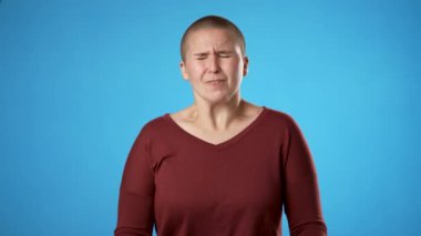 Öfkeli ümitsizliğin portresi, mavi arka planda izole edilmiş, çift cinsiyetli olmayan, genç bir kadının portresi.