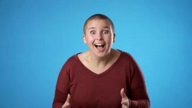 Çift cinsiyetli olmayan, 20 'li yaşlardaki değişken kadının şaşırmış portresi. Çekici bir kadın saf mavi arka planda izole edilmesine şaşırdı..