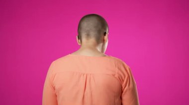 20 'li yaşlarda, çift cinsiyetli olmayan genç bir kadın. Arkasını dönüp kameraya bak. Stüdyoda pembe arka planda izole edilmiş bir jest portresi gibi başparmaklarını gösteriyor..