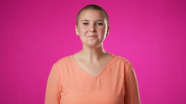 Mutlu bir cinsiyet değişkeni portresi. İkili olmayan, 20 'li yaşlarda, gülümseyen ve barış ve zafer işareti yapan pembe arka planda elleri olan genç bir kadın..