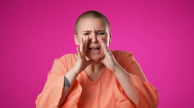 Çift cinsiyetli olmayan genç bir kadının portresi sinirli 20 'li yaşlarda, haykırıyor, elleri ağızda davet ediyor. Hey, pembe arka planda izole olmuşsun..