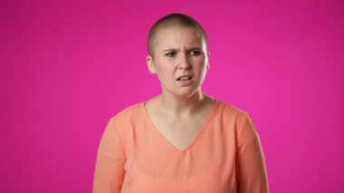 Çift cinsiyetli olmayan genç bir kadının portresi, 20 'li yaşlarda etrafınıza bakın parmaklarınızı dudaklarınıza koyun. Pembe arka plandaki stüdyo portresi yavaş çekimde izole edilmiş.