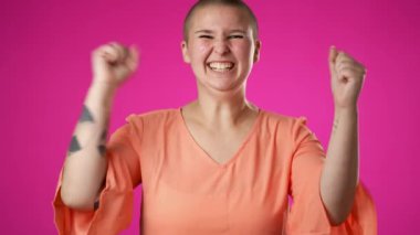 Heyecanlı, coşkulu, neşeli, genç, cinsiyet değiştiren, çift cinsiyetli olmayan, 20 'li yaşlarda, kazanan bir jest yapan, sıkı yumruklarını kutlayan, pembe arka plan stüdyo resmine izole edilmiş evet diyen, ağır çekimde.