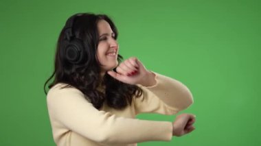 Kulaklık takan mutlu, genç bir kadın yeşil ekran arkasında yavaşça dans ediyor..