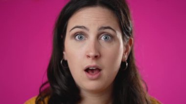 Şaşırmış 20 'li yaşlarda genç bir kadının yavaş çekim portresi. Çekici bir bayan pembe arka planda izole edilmesine şaşırdı..