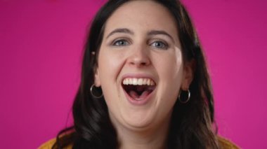 Yavaş çekim gülümseyen güzel esmer kadın 20 'li yaşlarda pembe arka plan stüdyosunda yalnız poz veriyor. İnsanlar samimi duygular, yaşam tarzı konsepti. Kameraya yakından bak.