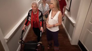 Yaşlı yaşlı bir anne, bir yürüteç kullanıyor, kızı, torunu ve kız arkadaşı tasmalı köpeğiyle bir aile ziyareti sırasında asansöre biniyor..