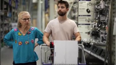 Erkek ve olgun kadın, inşaat projesini tartışmak için alışveriş arabasını hırdavatçıya götürüyor..