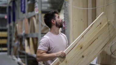 İnsan çam ağacını tutar ve taşır ve hırdavat dükkanının kereste alanına koyar..