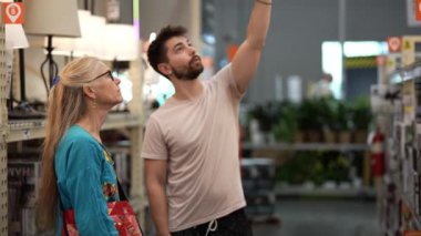 İnşaatçı erkek ve müvekkil yakınlaşması. Olgun kadın. Hırdavatçı dükkanının ışıklandırma bölümündeki ev yenileme projesi için malzemelere bak..