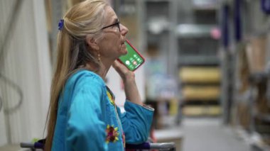 İnşaat projesi için kereste alırken hırdavatçıda telefonla konuşan olgun bir kadın..