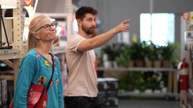 İnşaatçı erkek ve müvekkil olgun kadın nalbur dükkanının ışıklandırma bölümündeki ev yenileme projesine bakar.