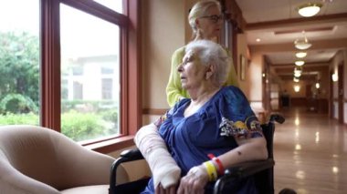 Olgun bir kadının yaşlı anneyi rehabilitasyon merkezinde iterken geniş açılı bir bakış açısı. Mutlu aile bakıcısı.