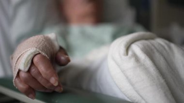 Hasta göğüs ve beyaz çarşaflarının bulanık geçmişiyle hastane yatağında sarılı bir elin yakın plan görüntüsü..