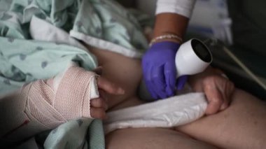 Bir tıp uzmanının ultrason taraması yaparken hastaların bandajlı görüntüsü. Hasta hastane yatağında yatıyor ve profesyonel doktor mor eldiven giyiyor..
