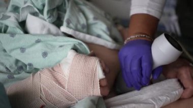 Hasta karnının ultrason sondasıyla yakından incelenmesi. Hasta hastane önlüğü giyiyor ve kolunda bandaj var. Eldivenli bir el sondayı tutar ve nazikçe bastırır.