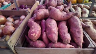 A closeup shot of two wooden crates filled with fresh produce. One crate contains plump yellow onions, while the other is stacked with large, vibrantly colored sweet potatoes.