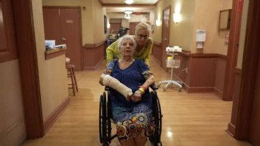 Aile kızı ziyaret ediyor, annesini rehabilitasyon merkezinde tekerlekli sandalyede itiyor..