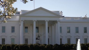 Beyaz Saray, Washington DC 'de, çiçek açan ağaçlarla çevrili, bahar mevsiminde parlak gökyüzünün altında Amerikan mimarisini sergiliyor..