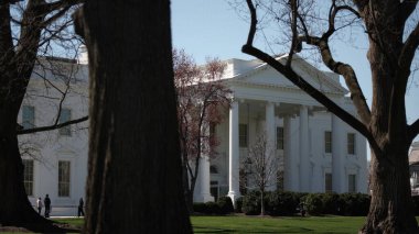 Beyaz Saray, ziyaretçilerin kıştan bahara Washington DC 'de tomurcuklanan ağaçlarla gezip geçişlerini gösterirken manzaranın önünde duruyor..