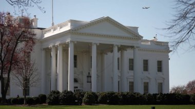Beyaz Saray, Washington DC 'de belirgin bir şekilde duruyor. Mavi gökyüzü ve ilkbahar yapraklarından oluşan bir zemin üzerinde sembolik mimarisini sergiliyor..