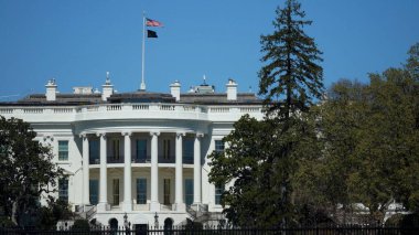 Washington DC 'deki açık gökyüzü ve canlı yeşillik kıştan bahara geçiş döneminde Beyaz Saray' ı çevrelemektedir. Amerikan bayrağı dimdik ayakta.