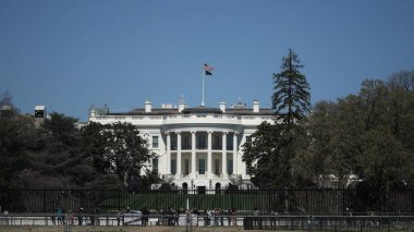 Ziyaretçiler, Washington DC 'deki Beyaz Saray' ın dışında açık bir bahar gününde mavi gökyüzünün altındaki ikonik mimari ve tarihi zemine hayran kalarak bir araya geldiler..