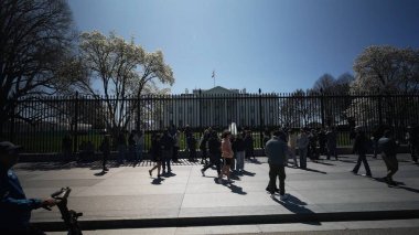 Beyaz Saray 'ın dışında toplanan kalabalık baharın güneşli bir gününde güzel havanın ve çiçek açan ağaçların tadını çıkarıyor. Federal bina arka planda duruyor..