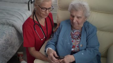 Bakıcı, yaşlı bir kadınla iletişim kurar ve ona sağlık merkezinde bir cihaz ile yardımcı olur. Ayarlama hafıza bakımını ve bağlılığı teşvik eder.