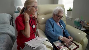 Bir bakıcı yaşlı bir kadınla iletişim kurar, anılarını paylaşır ve sohbete girişir, bir sağlık merkezinde bağlantı ve bakımı teşvik eder.