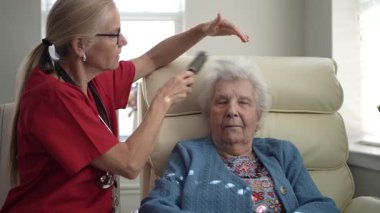 Bir bakıcı, sıcak ve rahatlatıcı bir ortamda yaşlı bir kadının saçını tarıyor, bir anlık ilgi ve rahatlığa odaklanıyor..