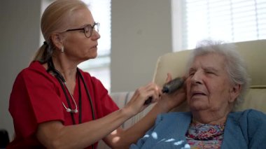 Bakıcı, yaşlı bir kadına sağlık merkezinde kibarca yardım eder, öğleden sonra kişisel bakım sırasında nişanını ve konforunu artırır..