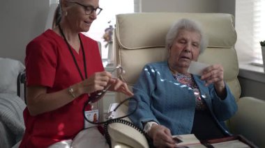 Bakıcı, sağlık merkezinde yaşlı bir kadınla dikkatlice iletişim kurar ve rahat bir ortamda bakım ve destek bağını gösterir..