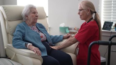 Bir bakıcı, yaşlı bir kadınla görüşür ve gün boyunca rahat bir sağlık merkezinde bakım ve destek sunar. Etkileşim, bağlantı ve konforu teşvik eder.