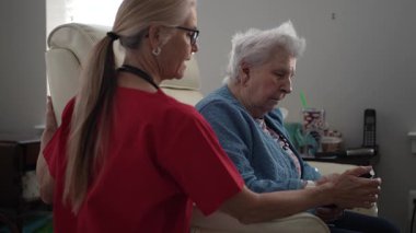 Bakıcı, sağlık merkezindeki yaşlı bir kadına destek sağlamaktadır. Anlamlı bir sohbete girişmişler, özen gösteriyorlar..