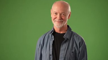 Olgun bir adam elleriyle kalp şeklini oluştururken sıcak bir şekilde gülümser. Dost canlısı bir tavır sergiliyor..