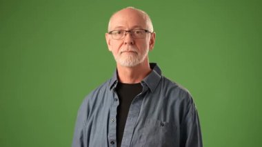 Olgun bir adam gülümsüyor ve dostça bir el sallıyor. Sıradan bir kıyafet giyiyor ve yeşil bir zemine karşı sıcak ve neşeli bir duygu taşıyor..