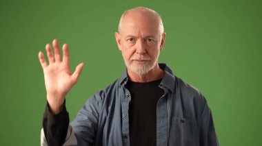 Olgun bir adam yeşil bir zemine karşı duruyor, elini kaldırıyor ve 