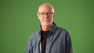 Gülümseyen kıdemli bir adamın portresi sağlam yeşil bir arkaplan karşısında güvenle izole edilmiş, neşeli bir gülümseme ve rahat bir tavırla..