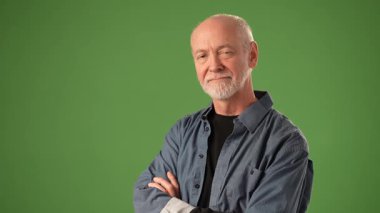 Olgun bir adam kollarını kavuşturup yeşil bir zemine karşı düşünceli bir ifade sergiliyor. Kıyafeti onun seçkin varlığına katkı sağlıyor..